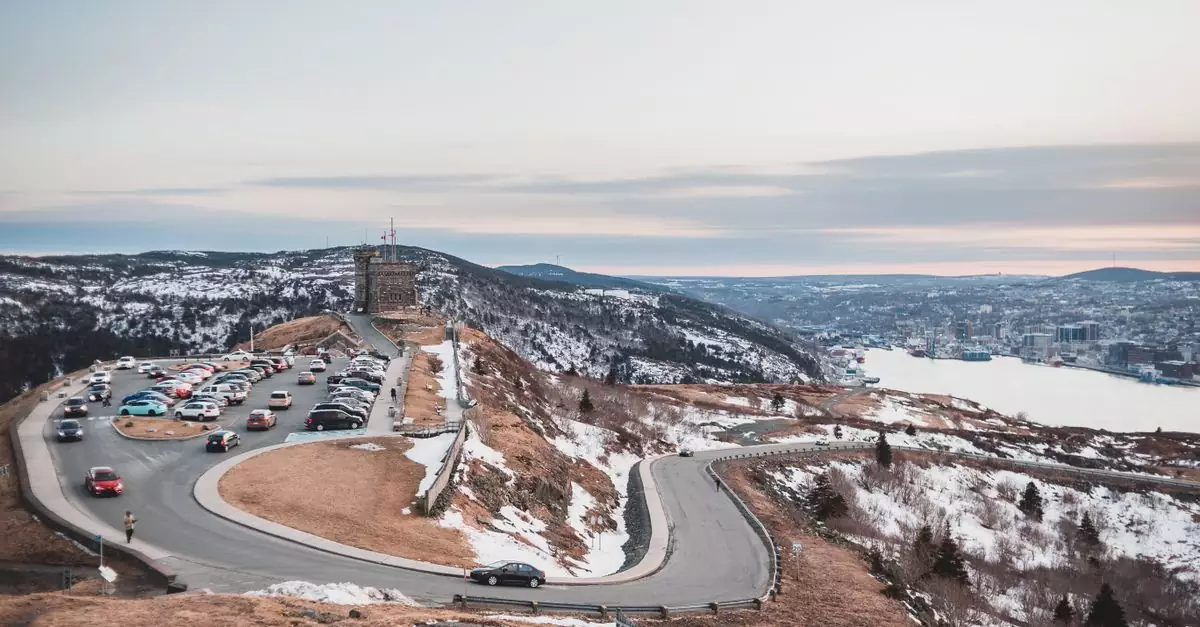 Automobiles riding on curvy asphalt roadway near grassy shore covered with snow against river and cloudy sky on winter day