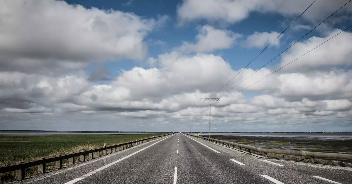 A scenic view of a straight road on Rømø Island, Denmark with dramatic clouds and coastal landscape.