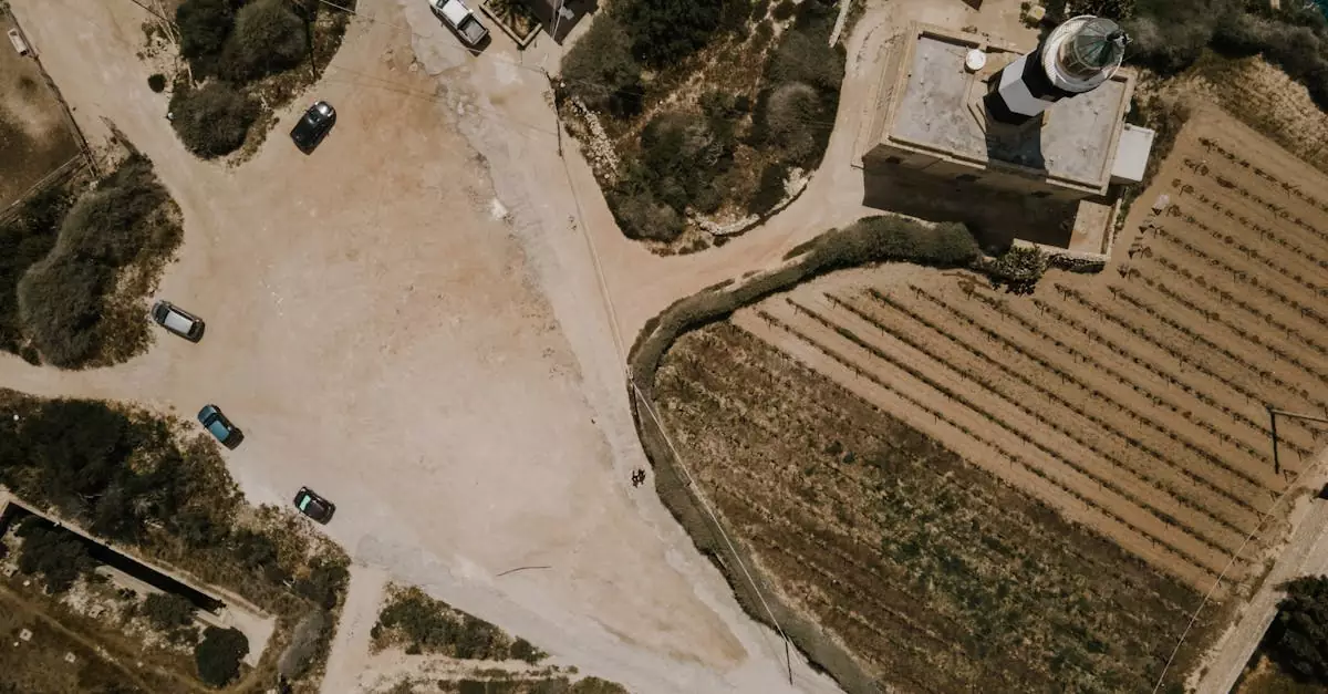 Drone photo capturing a lighthouse and surrounding fields in Marsaxlokk, Malta, with nearby roads and vehicles.