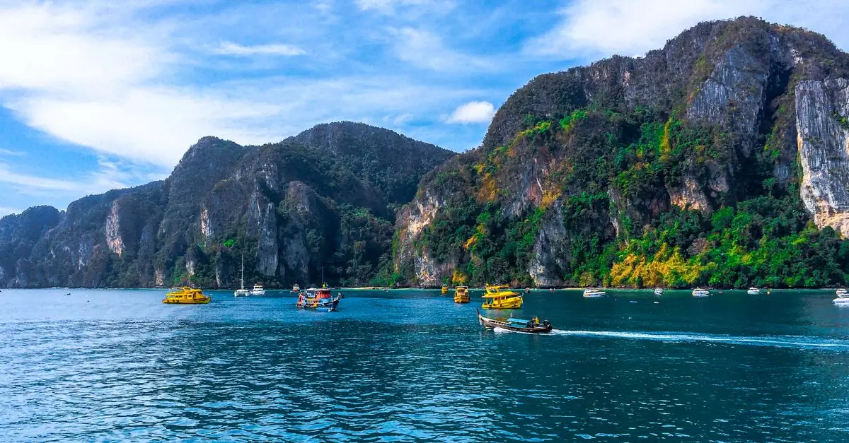 Colorful boats cruising along the Phi Phi Islands' stunning rocky coastline in Thailand, ideal for travel enthusiasts.