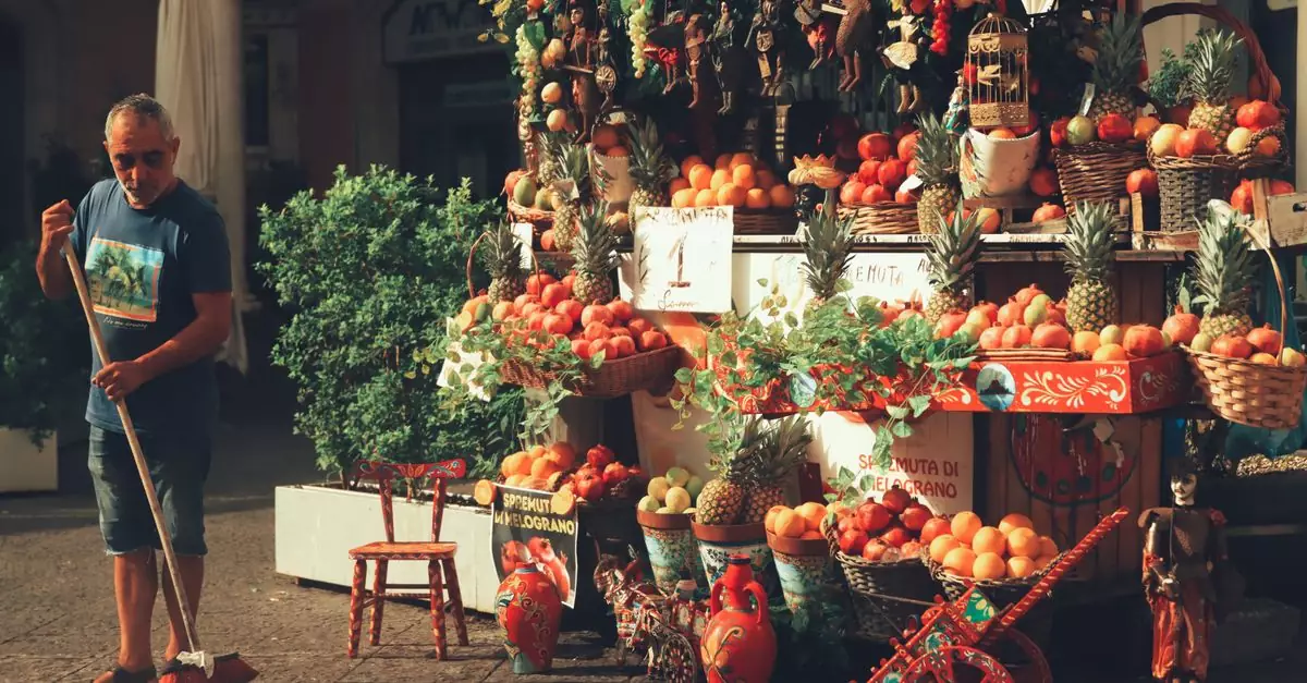 A man sweeps next to a colorful fruit stand in Catania's bustling market, Sicily, Italy.