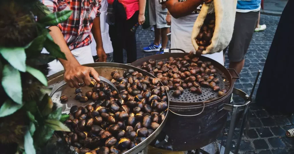 Street vendor roasting chestnuts over open fire in Rome, Italy market.