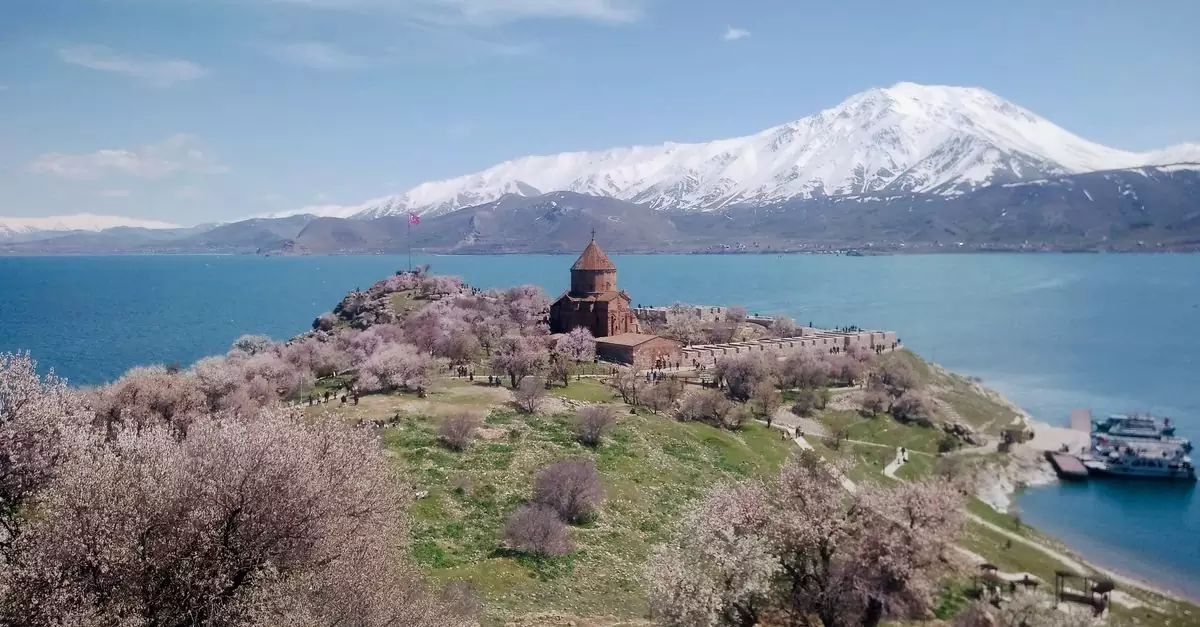 Scenic view of Armenian church on Lake Van with snowy mountains and spring blossoms.