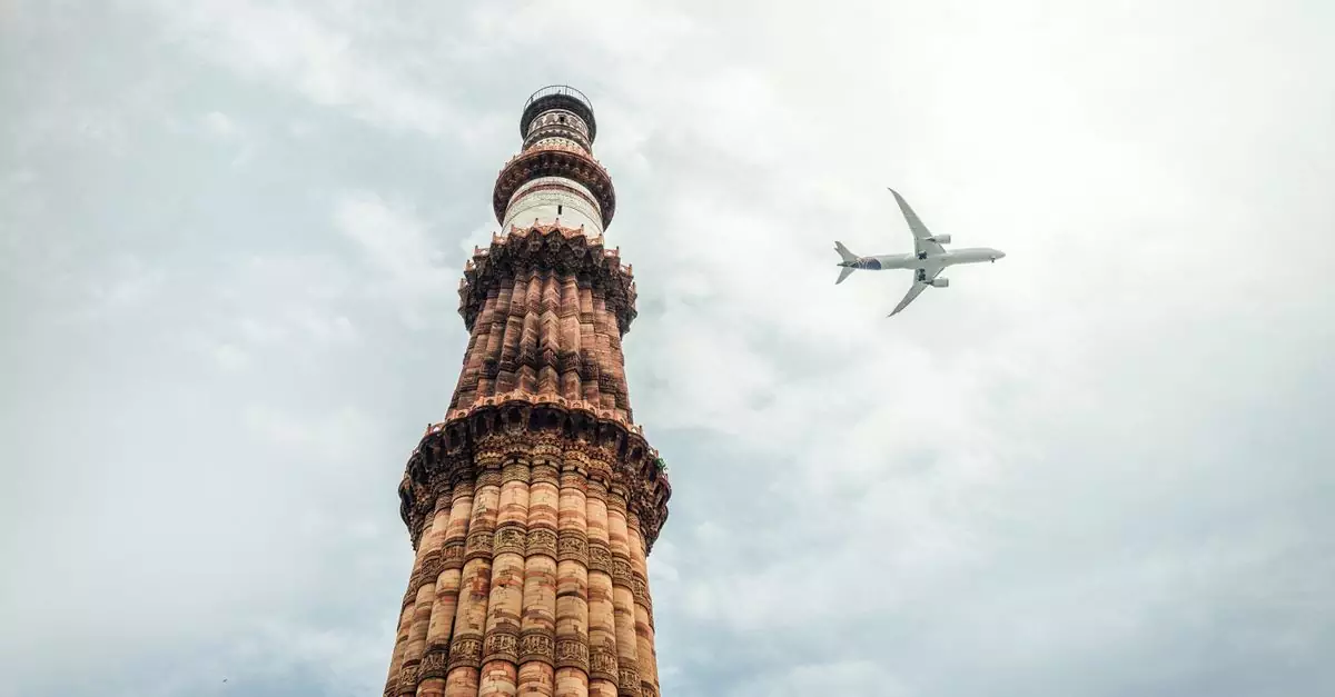 Stunning view of Qutub Minar with an airplane flying over against a cloudy sky in New Delhi, India.