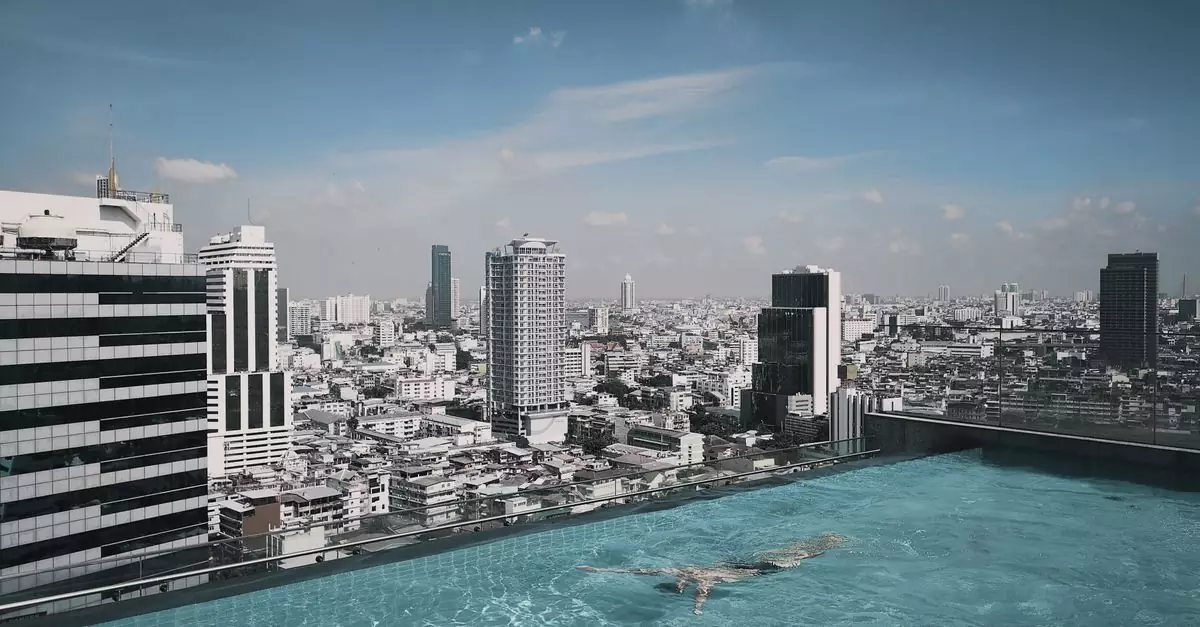 A serene rooftop infinity pool with a swimmer, overlooking the vibrant Bangkok skyline.