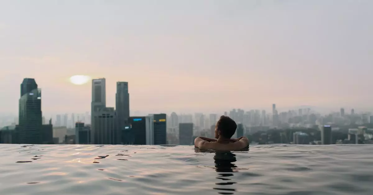 A man relaxes in an infinity pool with a breathtaking view of the Singapore city skyline at sunset.