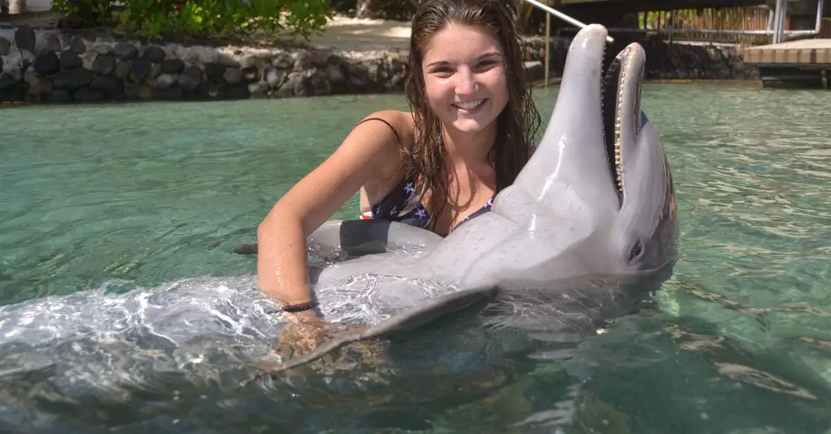 Smiling young woman swimming with a dolphin in clear tropical water.