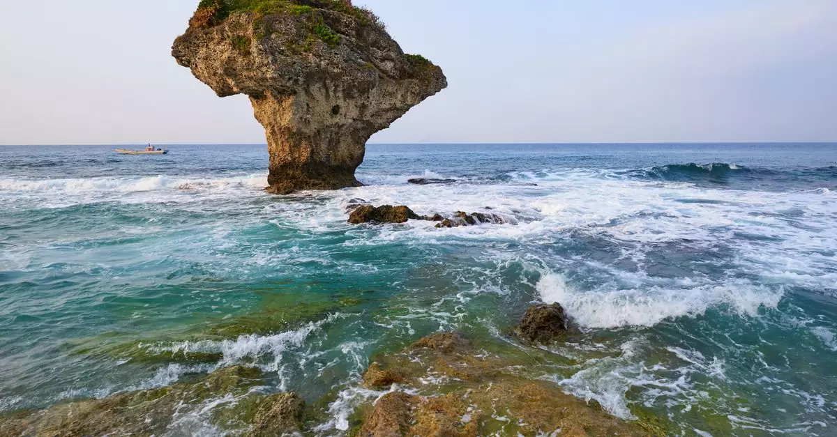 Stunning view of a unique rock formation in the sea with waves crashing at sunset.