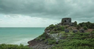 Historic Mayan ruins on a cliff with ocean view under a dramatic sky.
