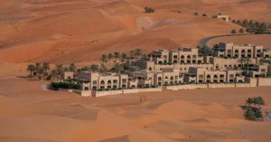 Explore the vast desert landscape of Abu Dhabi with this aerial view showcasing a luxurious hotel surrounded by sand dunes.