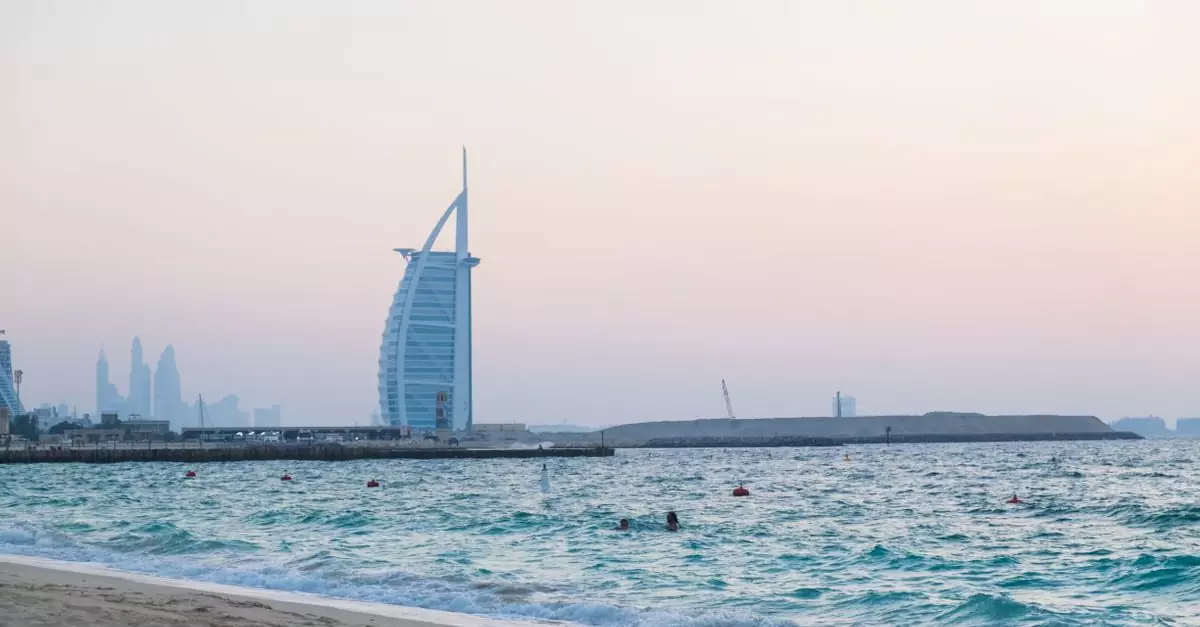 Picturesque scenery of sandy coast of waving sea and famous sail shaped building against cloudless sunset sky in Dubai