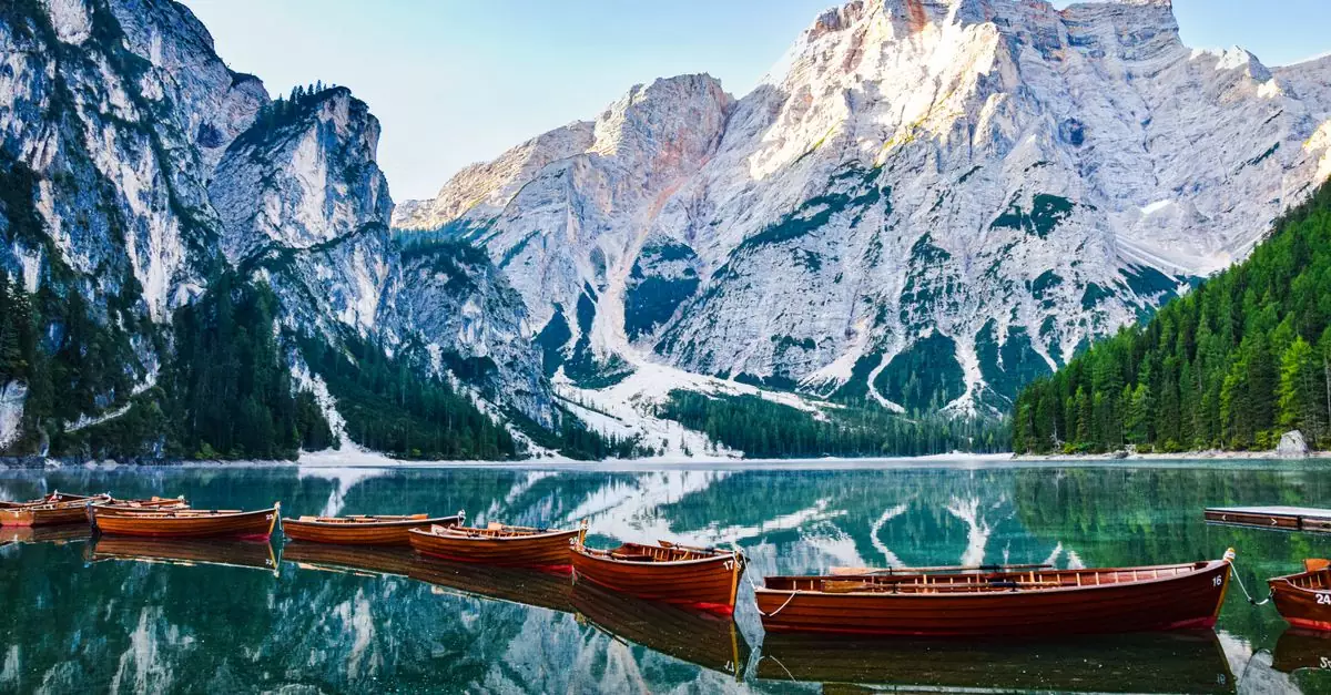 Stunning view of boats on a lake surrounded by Dolomite mountains and forest.
