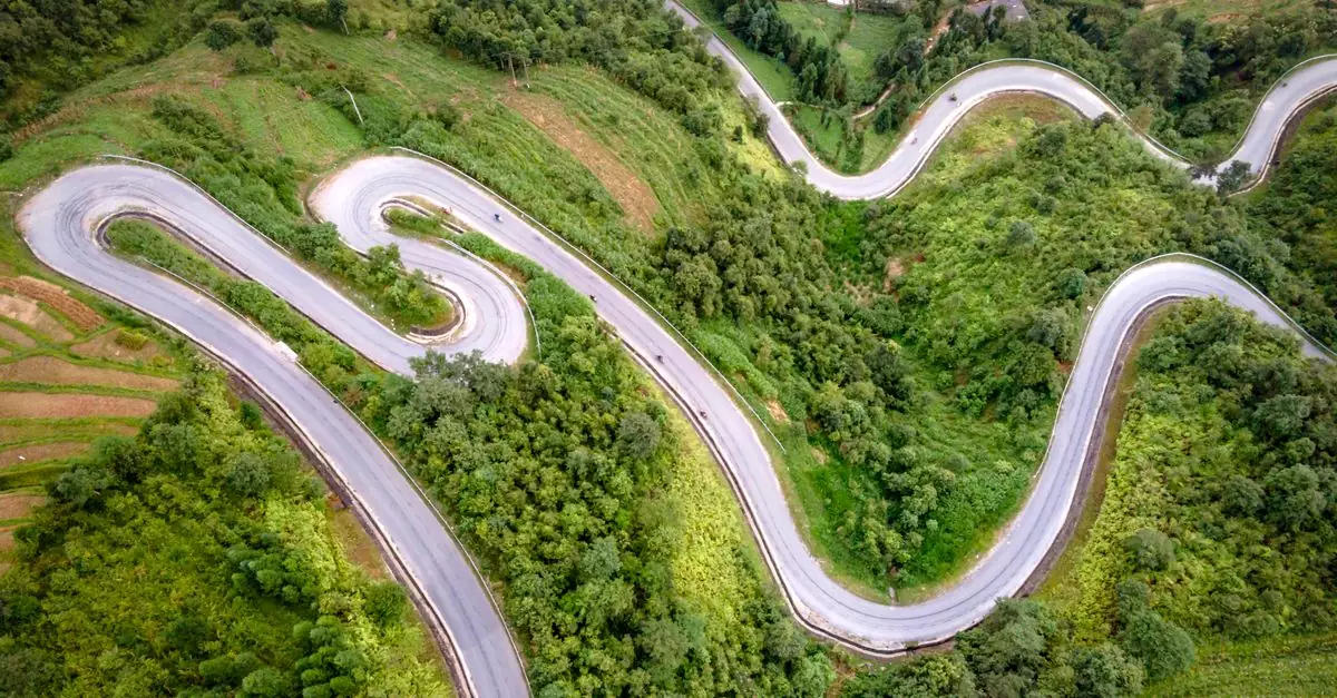 Aerial view of a winding mountain road amidst lush green nature, perfect for adventurous travels.