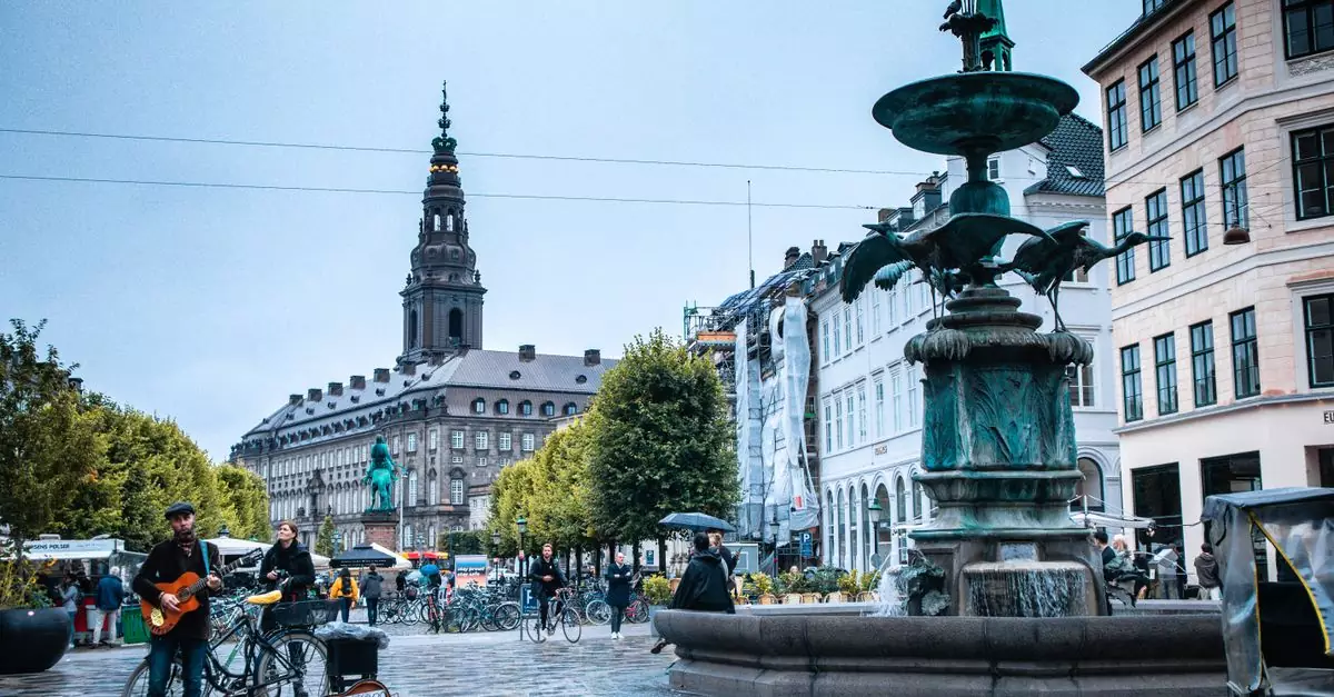 A street musician plays guitar by a fountain in Copenhagen city center, surrounded by urban architecture and pedestrians.