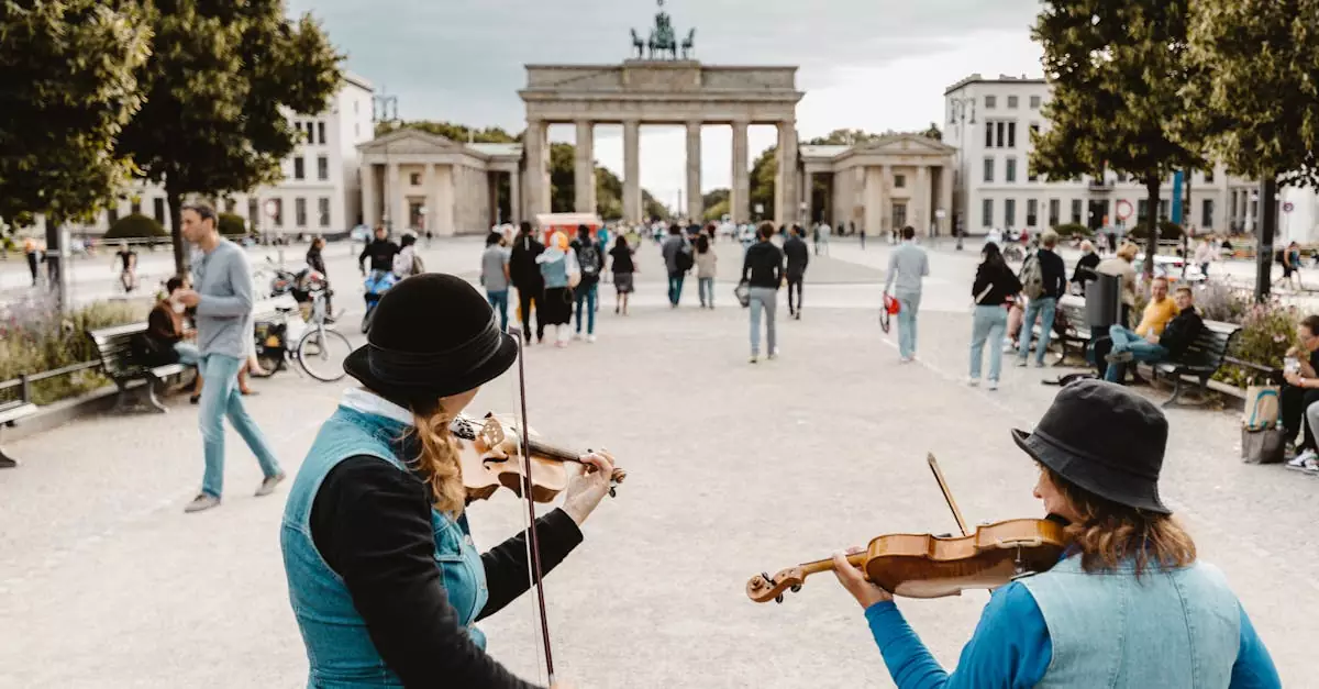 Two musicians play violins near Brandenburg Gate, Berlin, with people strolling by.