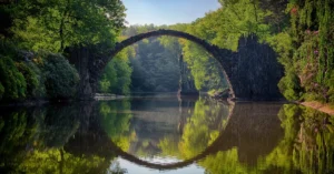 Capture of the iconic Rakotzbrücke reflecting in calm waters amidst lush greenery in Germany.