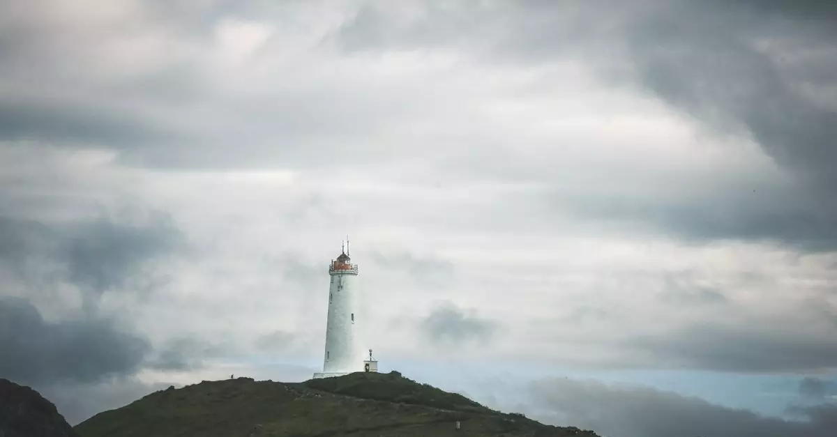 A solitary lighthouse stands against dramatic clouds on an Icelandic landscape.