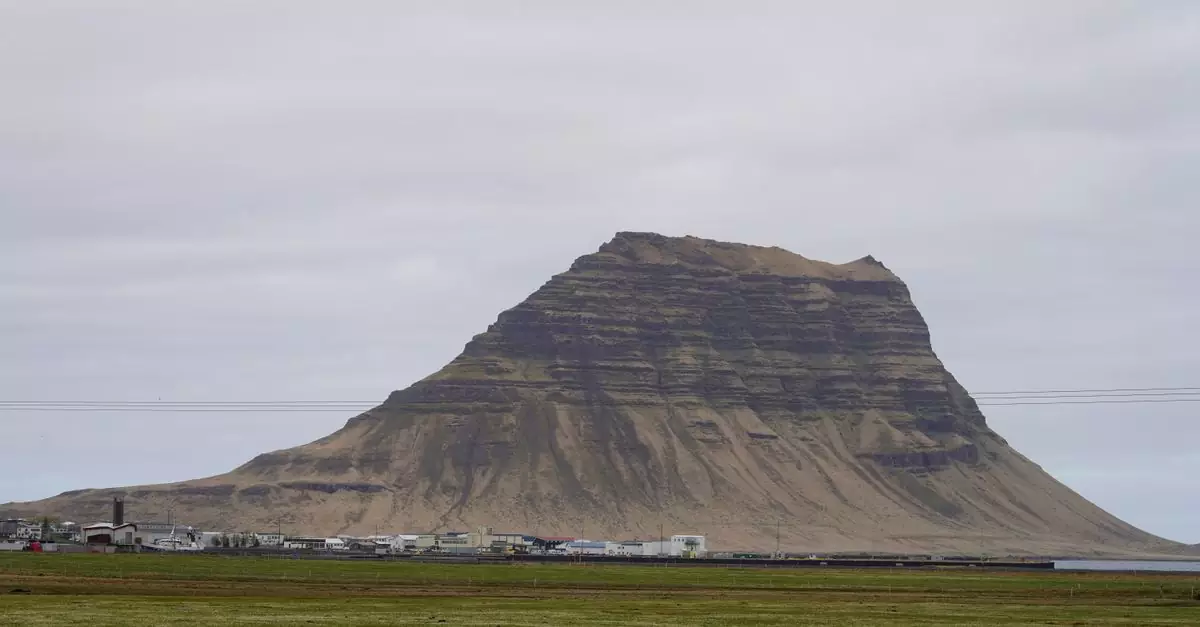 Stunning view of Kirkjufell Mountain under a cloudy sky in Iceland, highlighting its unique shape and the surrounding landscape.