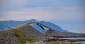 A stunning view of the curved bridge on the Atlantic Ocean Road, Norway, with scenic mountains in the background.