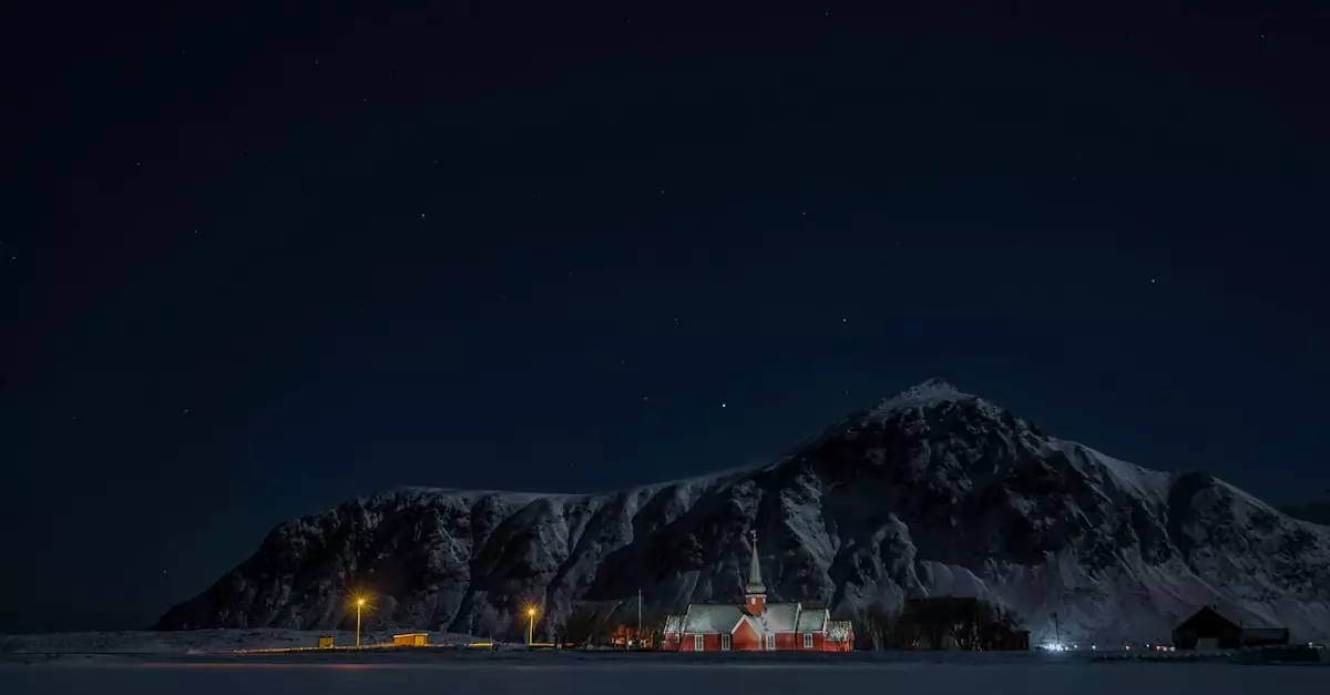 Scenic view of Flakstad Church surrounded by mountains under a starry night sky in Nordland, Norway.