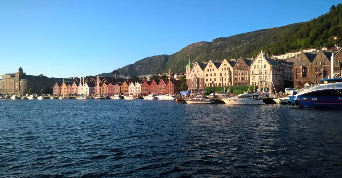Charming pastel-colored houses line Bergen's harbor, Norway, under a clear summer evening sky.