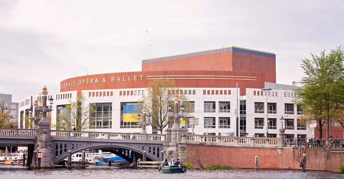 Amsterdam Opera House with distinctive architecture by a canal bridge under a bright sky.