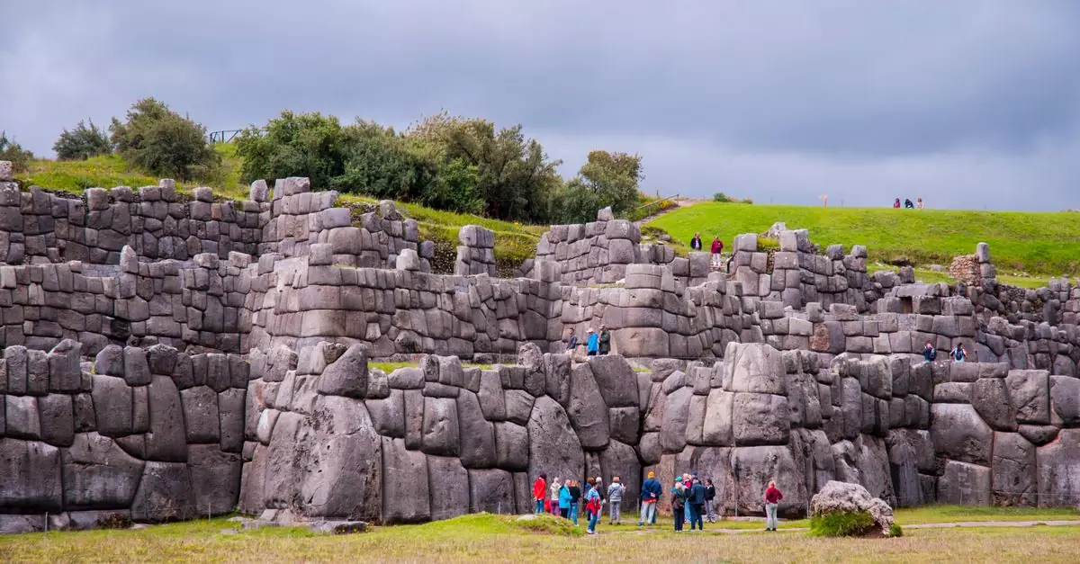 Tourists exploring the ancient stone walls of Sacsayhuamán in Cusco, Peru under a cloudy sky.