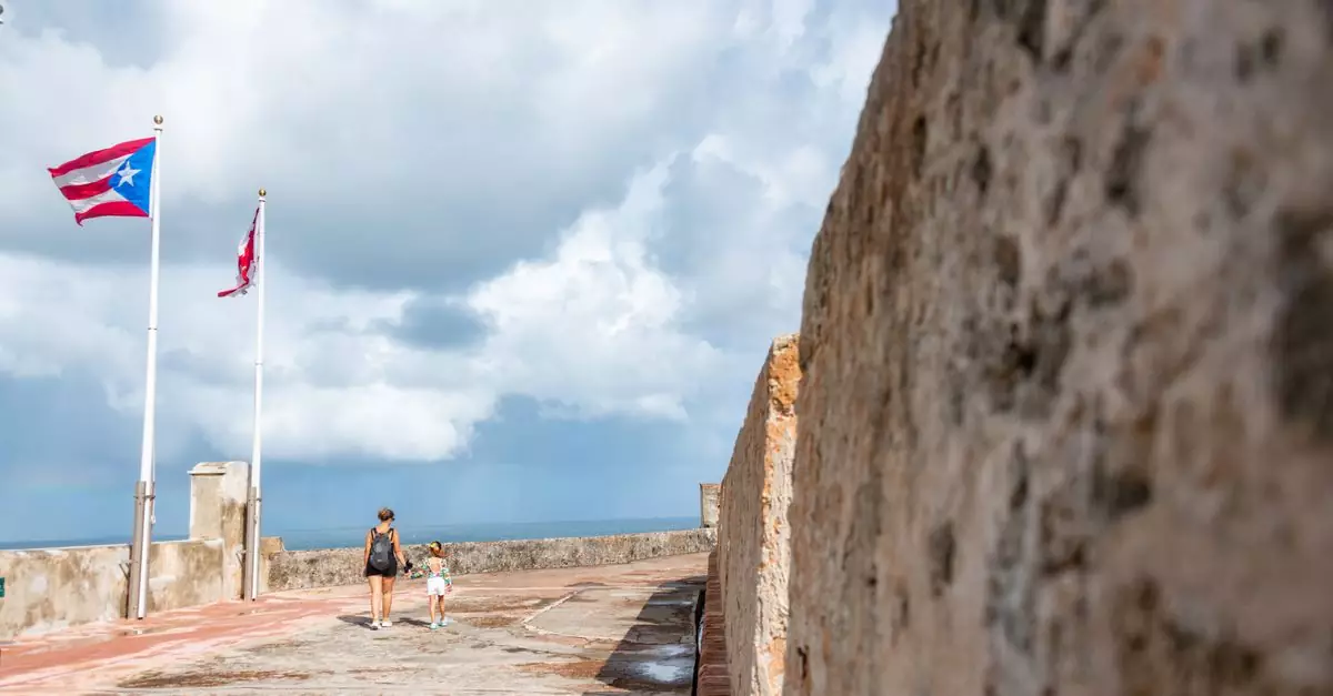 A mother and daughter walk along El Morro fortress with flags in the breeze, under a cloudy sky.