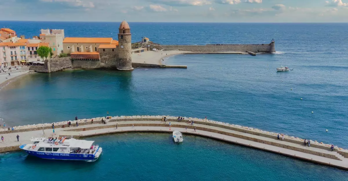 Scenic aerial view of Collioure's harbor with its iconic lighthouse and historic church under a bright sky.