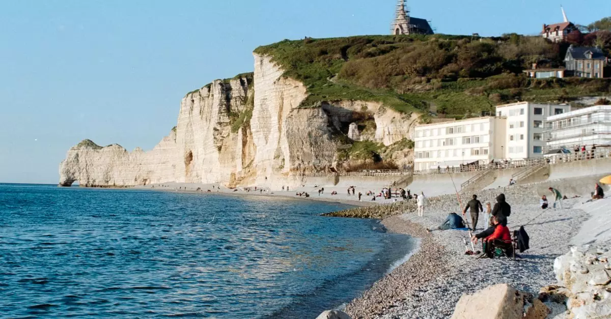 A picturesque view of Étretat's cliffs and beach in Normandy, France, with people strolling along the shore.