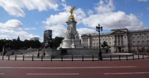 View of the Victoria Memorial with Buckingham Palace in the background under a bright blue sky.