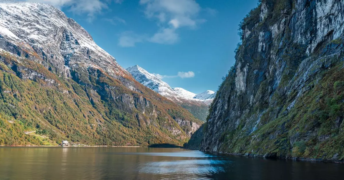 Breathtaking view of a Norwegian fjord with snow-capped mountains and clear blue skies.