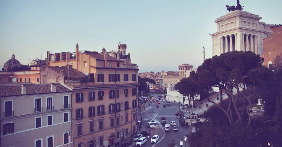 Various cars driving on asphalt road near aged residential buildings and famous Victor Emmanuel II Monument against cloudless blue sky in Rome
