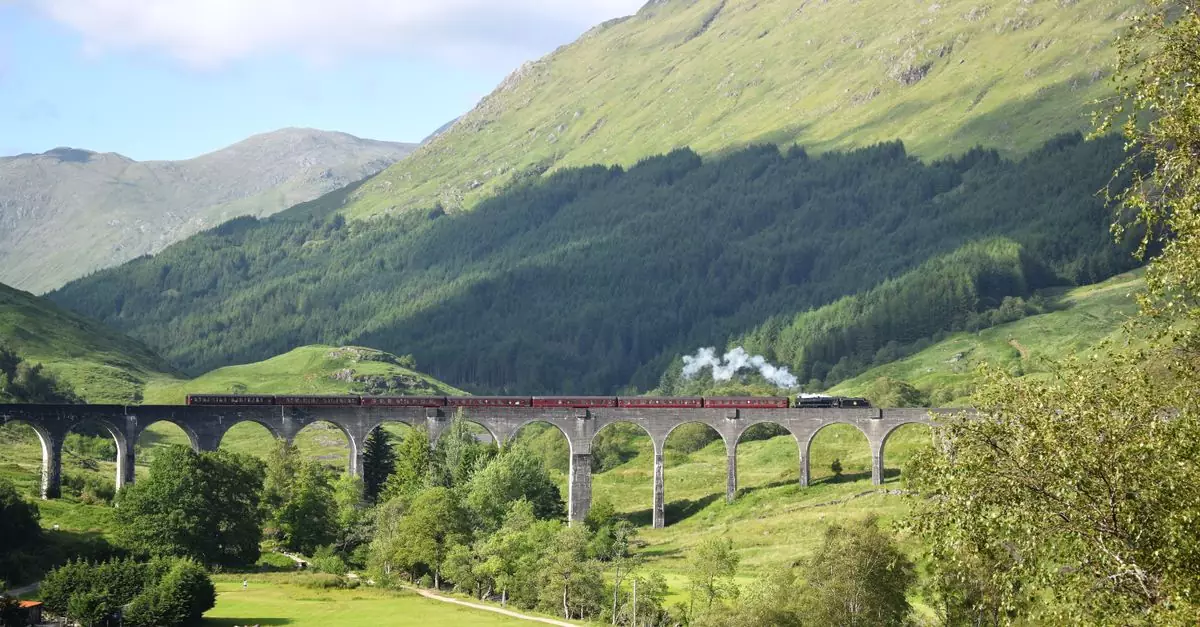 Steam train crossing the iconic Glenfinnan Viaduct in Scotland's lush green Highlands.