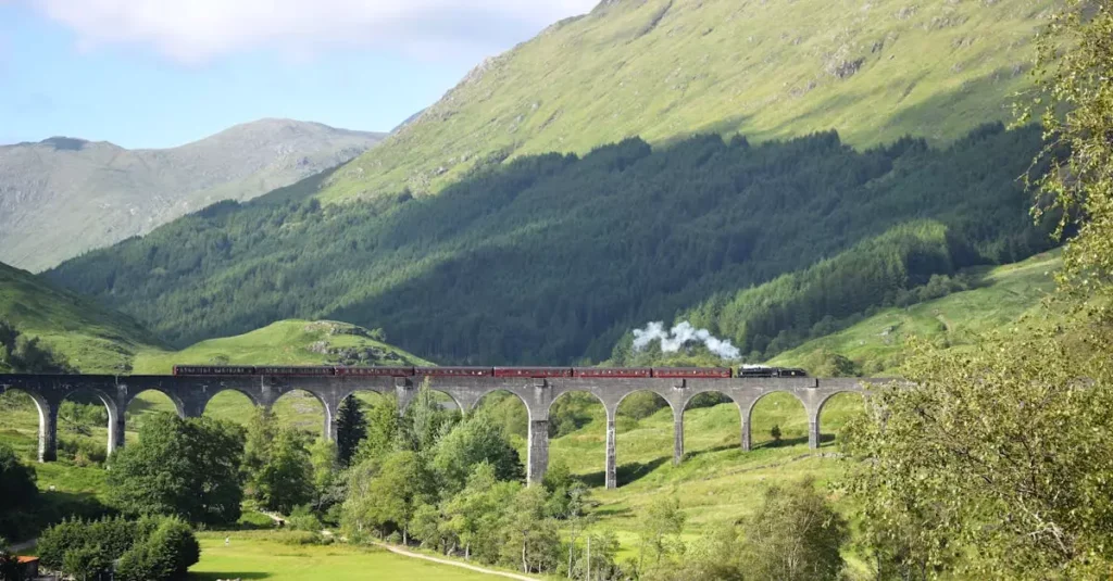Steam train crossing the iconic Glenfinnan Viaduct in Scotland's lush green Highlands.