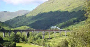 Steam train crossing the iconic Glenfinnan Viaduct in Scotland's lush green Highlands.