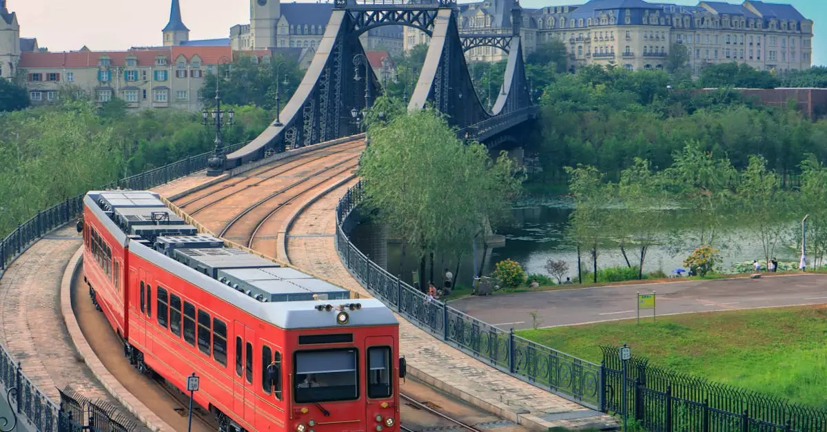 A vibrant red train crossing a historic bridge with a scenic view of a city in the background.