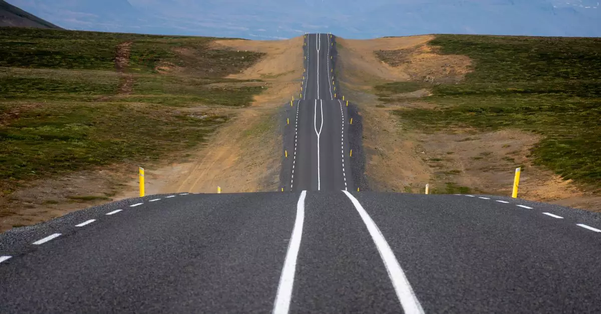 A long, empty road stretches through the scenic and remote Icelandic mountains, capturing nature's vastness.