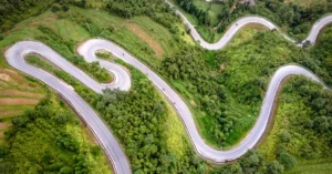 Aerial view of a winding mountain road amidst lush green nature, perfect for adventurous travels.