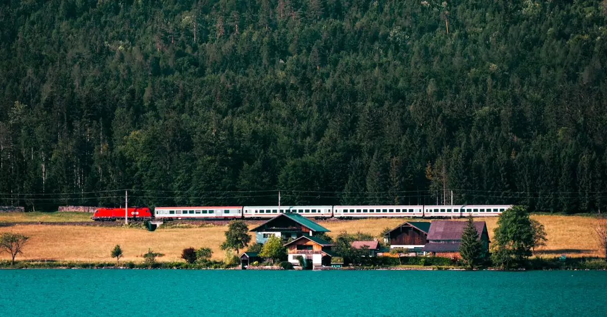 Picturesque view of a train passing by Hallstatt lake with forest and houses in the background.