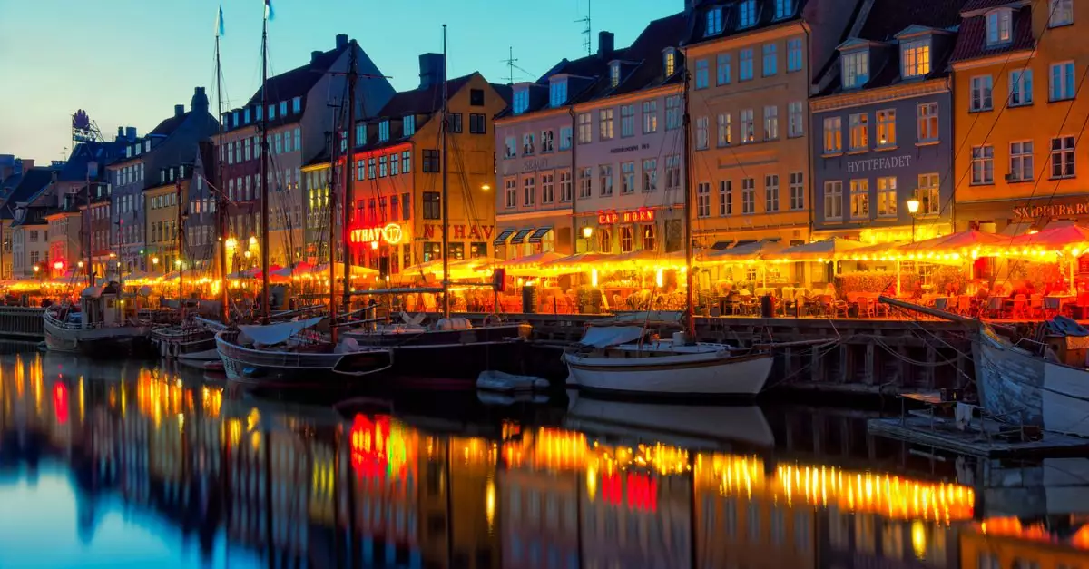 Beautiful view of Nyhavn Canal with illuminated buildings and boats at dusk in Copenhagen, Denmark.