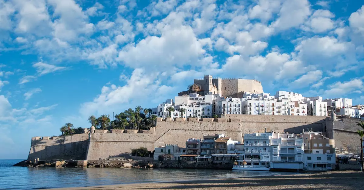 Scenic view of Pe&ntilde;&iacute;scola Castle beside a sunny beach under a vibrant sky.