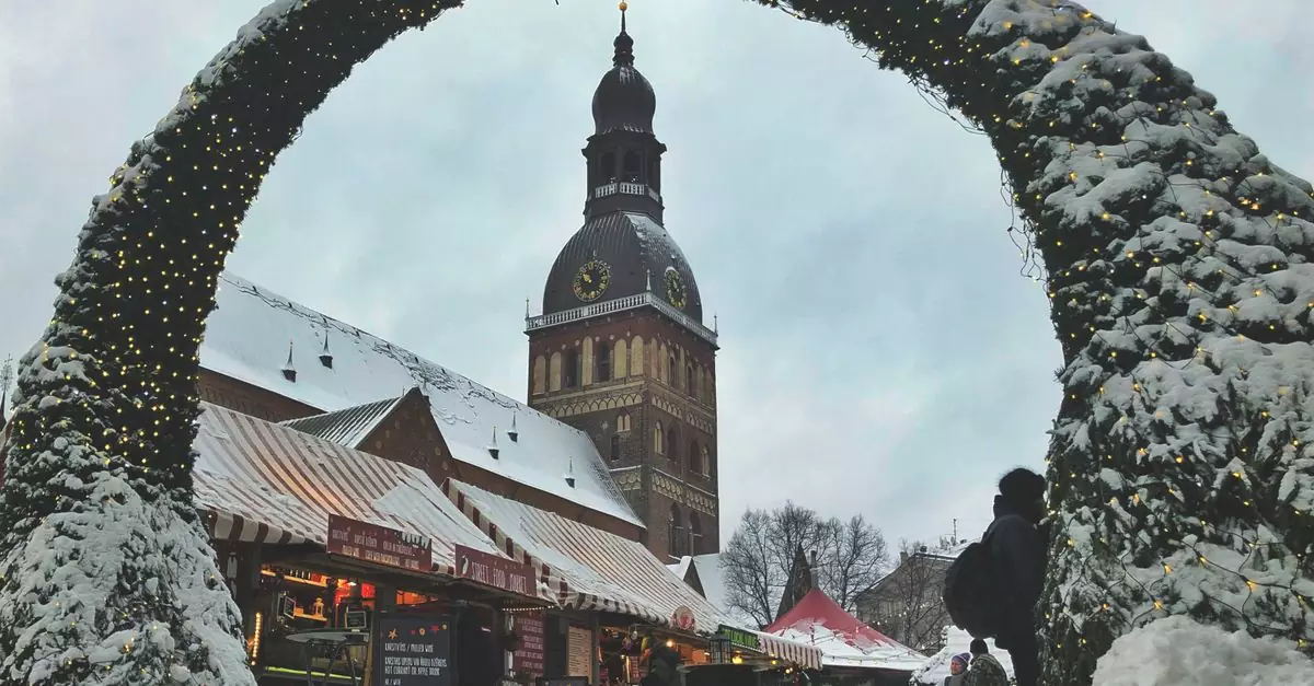Snow-covered market with illuminated arch and cathedral tower, capturing winter's charm.