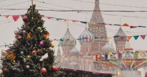 A snowy festive scene with a Christmas tree and St. Basil's Cathedral in Moscow, Russia.