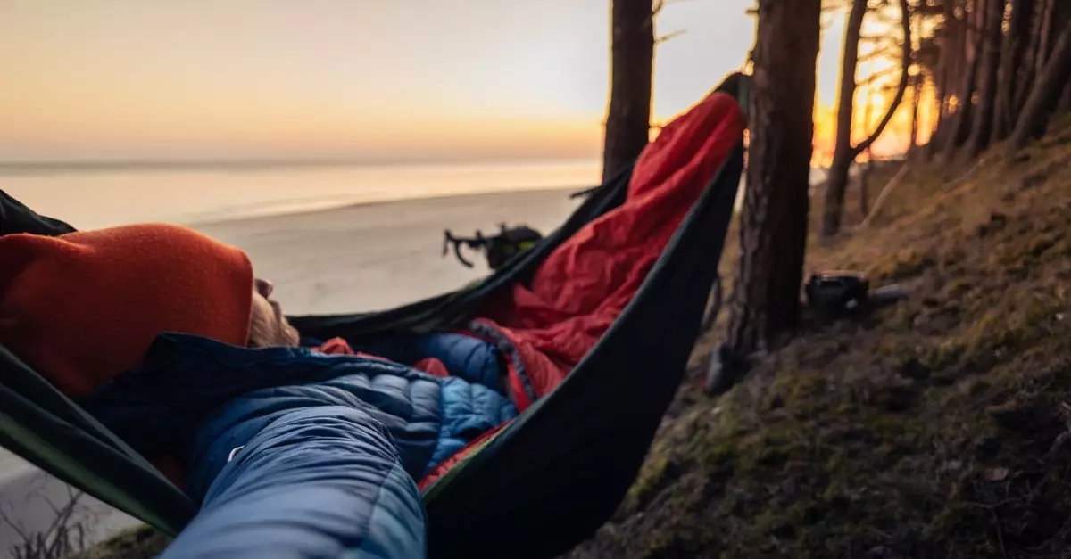 Person sleeping in hammock on forested beach at sunset, enjoying outdoor leisure.