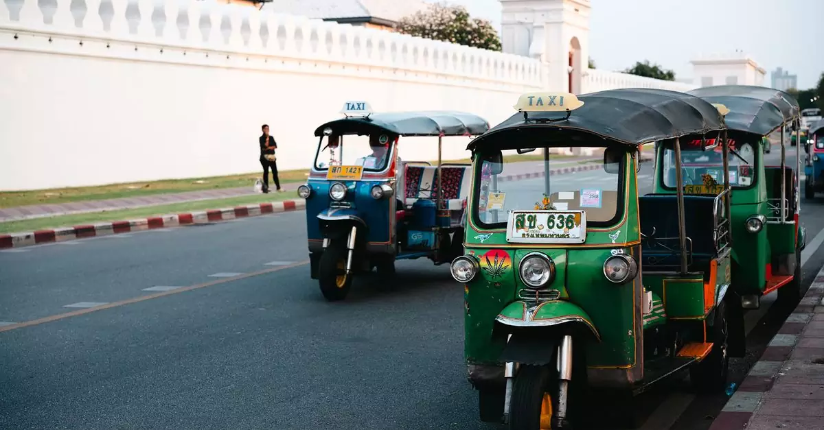 Classic green and blue tuk-tuks parked by a white wall in Bangkok, capturing local street culture and transportation.