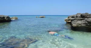 A person snorkeling in crystal clear tropical waters surrounded by rocky formations and a vast serene ocean.