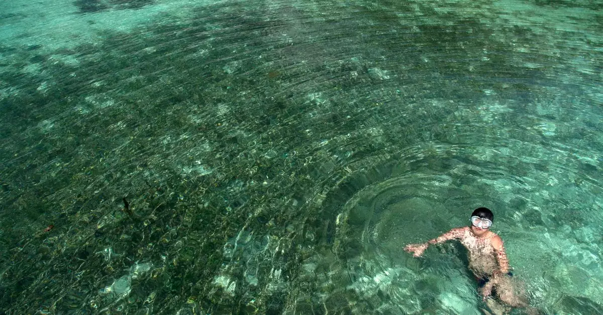 Man swimming in clear turquoise water with a snorkel, creating ripples.