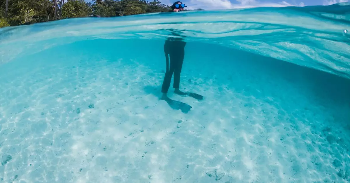 Unrecognizable person in snorkeling mask and goggles standing in transparent blue seawater in tropical nature on sunny clear day