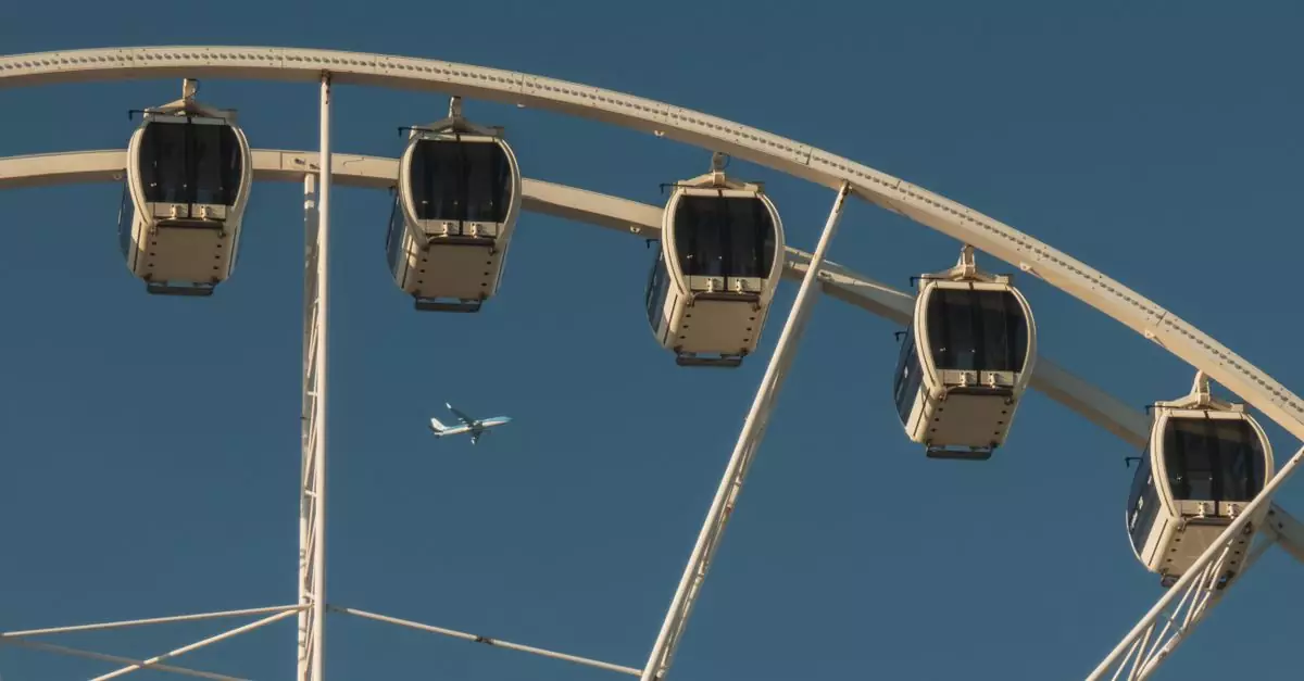 Close-up of a Ferris wheel with an airplane flying against a clear blue sky.